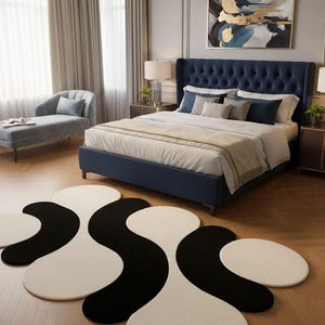 May include: A bedroom scene featuring a navy blue upholstered bed with a tufted headboard, layered bedding, and decorative pillows. A black and white abstract rug is on the hardwood floor. A chaise lounge and artwork complete the room.