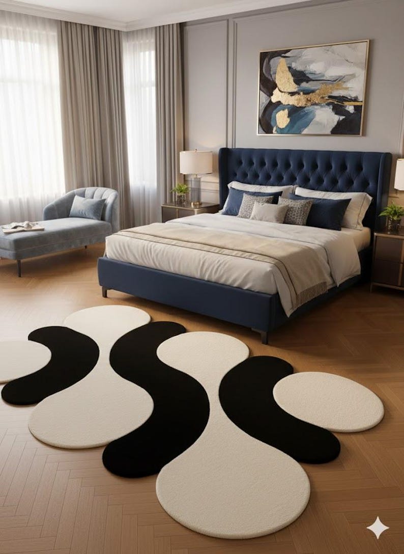 May include: A bedroom scene featuring a navy blue upholstered bed with a tufted headboard, layered bedding, and decorative pillows. A black and white abstract rug is on the hardwood floor. A chaise lounge and artwork complete the room.
