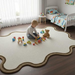 May include: A cream-colored, irregularly shaped rug with a brown border. A young child is playing with wooden blocks and a teddy bear on the rug. A white bed with dinosaur-themed bedding is in the background.
