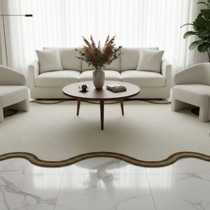 May include: A modern living room setup featuring a cream-colored sofa, two matching armchairs, and a round wooden coffee table. A unique, cream-colored rug with a brown border sits on a marble floor, creating a cozy and stylish space.