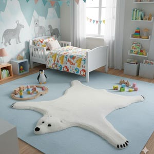 Pode incluir: Um quarto infantil com uma cama branca, roupa de cama colorida e um tapete azul claro. Um tapete branco em forma de urso polar está no chão. O quarto é decorado com arte de parede com tema de animais e um brinquedo de pinguim. Um comboio de madeira e blocos coloridos também estão presentes.