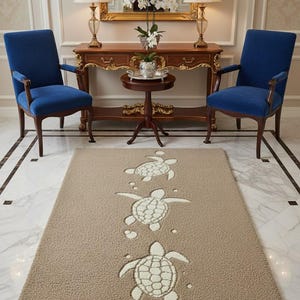 May include: A rectangular area rug with a textured beige surface featuring three white sea turtle motifs arranged in a vertical line. The turtles are depicted with detailed shell patterns and small circular bubbles surrounding them on the rug's surface.