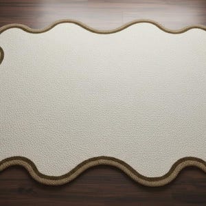May include: Cream-colored, cloud-shaped rug with a textured surface and a brown border. The rug is placed on a dark wooden floor. This decorative rug adds a soft touch to any room.