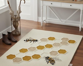 May include: Cream-colored rectangular rug with a honeycomb pattern and two embroidered bees. The honeycomb design features shades of gold and beige. The rug is placed on a wooden floor, creating a warm and inviting atmosphere.