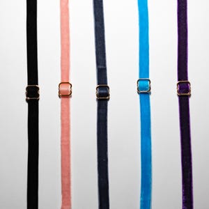 May include: Five velvet straps in black, peach, navy, turquoise, and purple, each with a gold-coloured metal adjuster. The straps are arranged vertically against a light background, showcasing the variety of colours and textures.