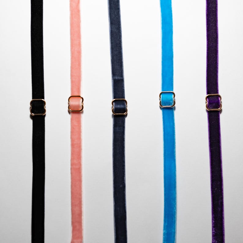May include: Five velvet straps in black, peach, navy, turquoise, and purple, each with a gold-coloured metal adjuster. The straps are arranged vertically against a light background, showcasing the variety of colours and textures.