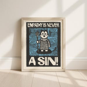 Puede incluir: Impresión artística enmarcada con un personaje de dibujos animados sosteniendo un tridente, sobre un fondo azul y negro. El texto "EMPATHY IS NEVER A SIN!" se muestra en negrita, en letras negras. La obra de arte está en un marco de madera de color claro.