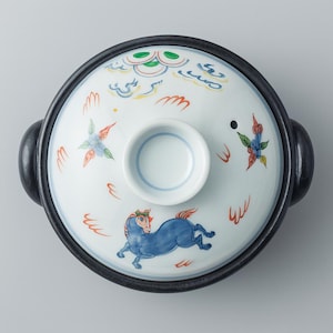 以下が含まれることがあります： 青い馬の模様が施された蓋付きの陶器の鍋。蓋は白で、雲や花の模様など、カラフルなアクセントが施されています。鍋には黒い縁と取っ手が付いています。
