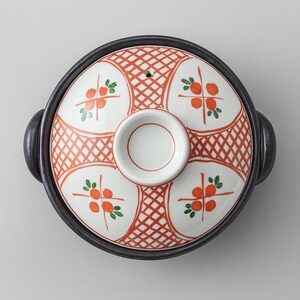 May include: Round ceramic cooking pot with a black rim and handles. The lid is white with a red lattice pattern and orange fruit designs. The lid has a white circular handle in the center.