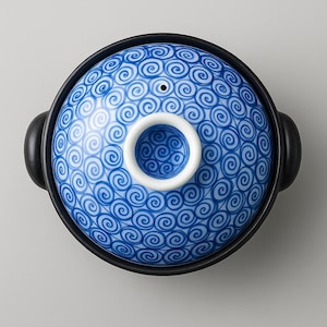 May include: Overhead view of a black and blue ceramic cooking pot. The lid is blue with a white spiral pattern. The lid has a white handle and a small hole. The pot has two black handles on either side.