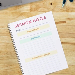 May include: A white notebook with a pink title "SERMON NOTES" and sections for date, bible passage, key points, and reflection & prayer. The notebook is on a wooden surface with a laptop, mouse, and pens.