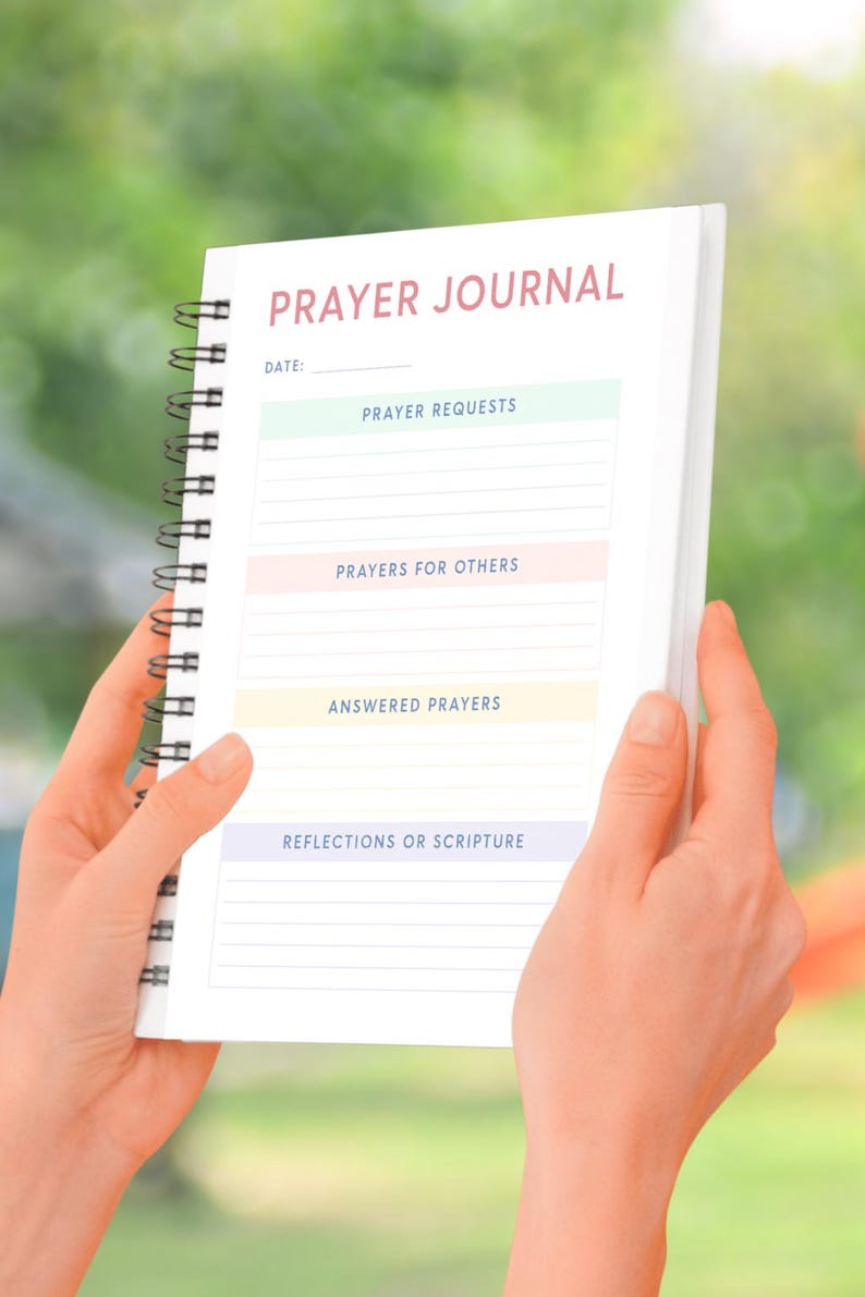 May include: A white prayer journal with a black spiral binding. The cover has the words "PRAYER JOURNAL" in pink lettering. The journal has sections for "Prayer Requests", "Prayers for Others", "Answered Prayers", and "Reflections or Scripture".