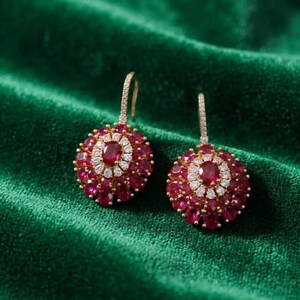Puede incluir: Un par de pendientes colgantes de oro con una piedra roja central de talla ovalada rodeada por un halo de pequeñas piedras blancas, con una capa exterior de piedras rojas ovaladas más grandes en un diseño de racimo circular.