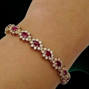 Peut inclure: Un bracelet en or orné de pierres précieuses rouges de forme ovale et de petites pierres blanches. Le bracelet est serti dans un métal doré et est présenté sur un bras. Les pierres sont disposées en motif floral.