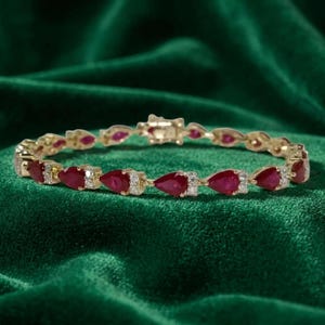 Può includere: Un bracciale in oro caratterizzato da una serie di rubini rossi a forma di pera che si alternano a piccoli diamanti rotondi e trasparenti. Il gioiello è dotato di una chiusura di sicurezza e presenta un motivo ripetuto di gemme incastonate in oro.