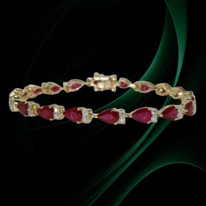Può includere: Bracciale in oro con pietre preziose rosse a forma di pera e piccoli accenti bianchi. Il bracciale ha un design delicato con una chiusura sicura. Le pietre sono uniformemente distanziate lungo la fascia d'oro.