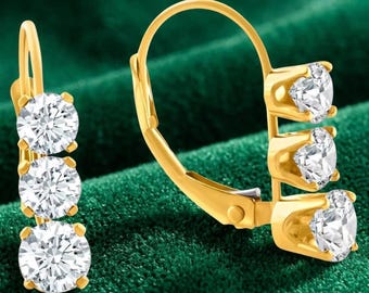 May include: A pair of gold leverback earrings, each featuring three round, clear, faceted stones arranged in a vertical line. The metal settings are polished gold, and the stones are secured with four-prong settings in a classic drop design.