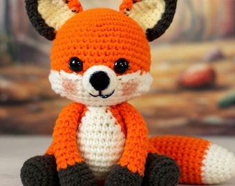 May include: A handmade crochet fox toy in orange, white, and black. The fox has large black eyes, a white chest, and a fluffy tail. The fox is sitting with its legs outstretched.