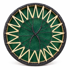 May include: A circular frame drum featuring a vibrant green drumhead surface. The outer edge is wrapped in black material, while the center is tensioned with a complex lacing system made of light tan strips and thin black cordage in a star pattern.