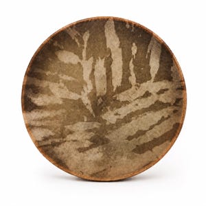 May include: A circular frame drum with a wooden rim and a natural skin head. The drum head features a mottled, earthy brown and beige pattern with organic, leaf-like shapes across the surface, creating a textured appearance on the drum skin.