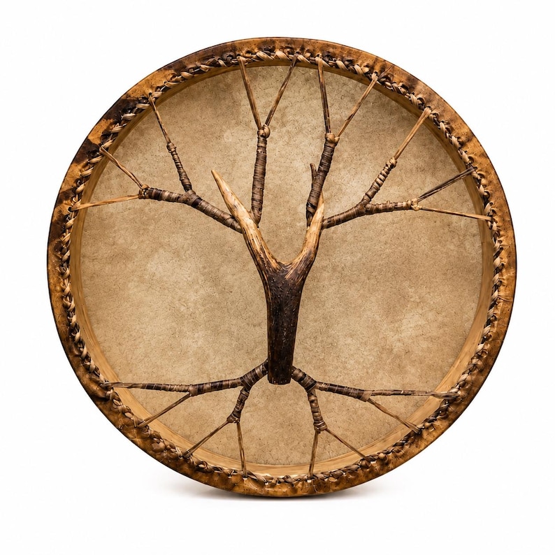 May include: A circular frame drum featuring a tan drumhead made of stretched hide. A central wooden branch structure is secured to the drumhead with thin, dark brown cordage that radiates outward to the wooden rim, which is wrapped in braided leather.