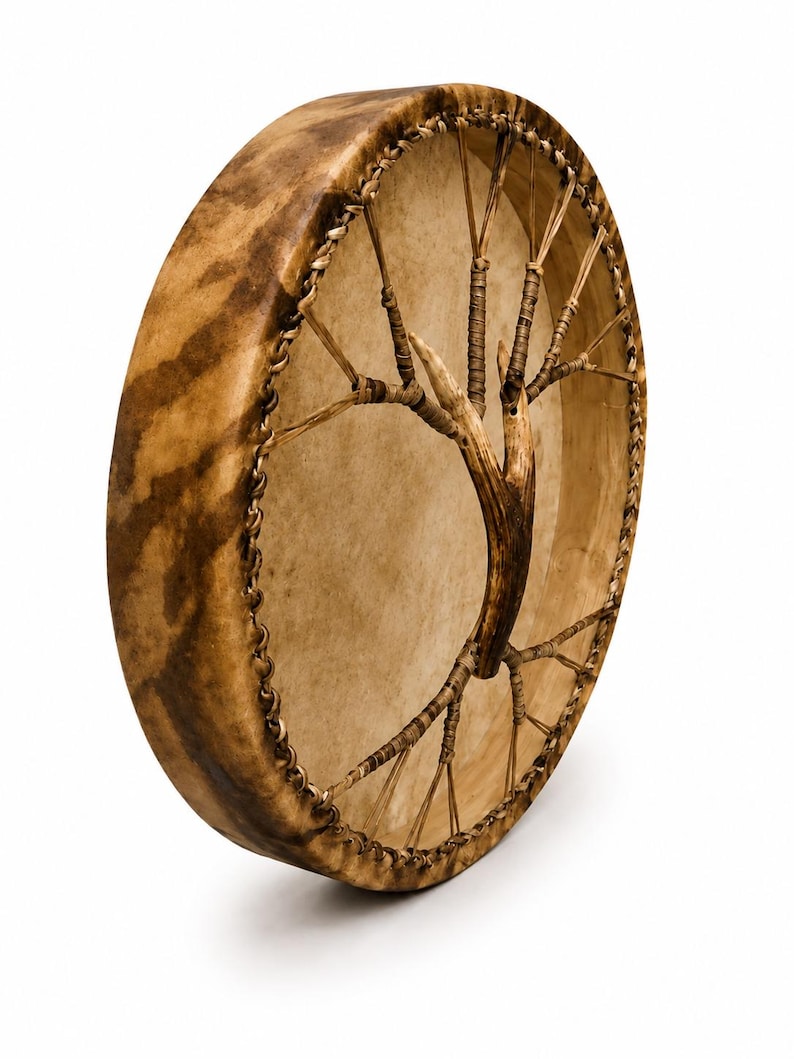 May include: A round frame drum with a light tan drumhead and a dark brown mottled wooden frame. The drum features a central handle shaped like a tree branch, connected to the frame by thin, light-coloured cord lacing around the entire perimeter.