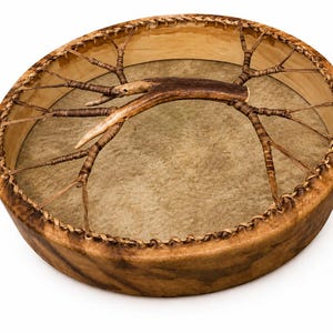 May include: A round frame drum with a light brown animal hide head stretched over a wooden hoop. The drum features a central handle made from a natural brown antler, which is connected to the frame by thin, woven leather lacing strips.
