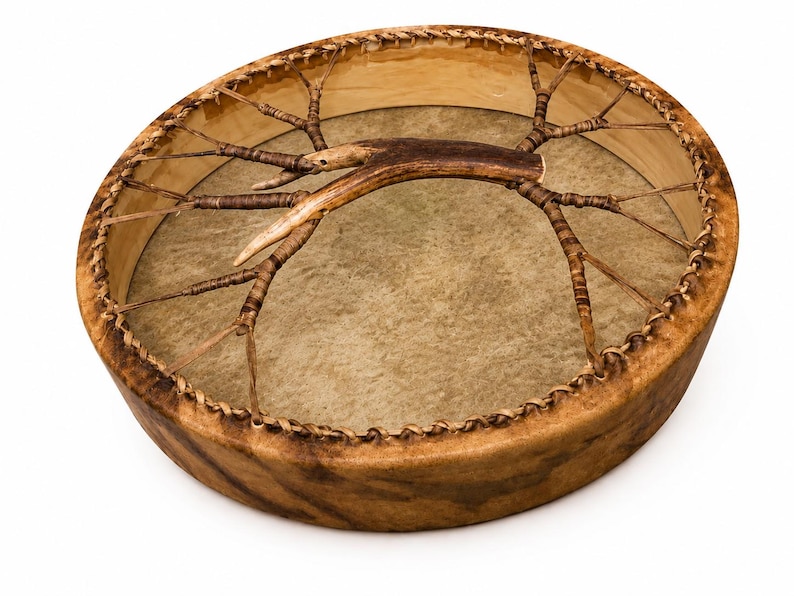 May include: A round frame drum with a light brown animal hide head stretched over a wooden hoop. The drum features a central handle made from a natural brown antler, which is connected to the frame by thin, woven leather lacing strips.