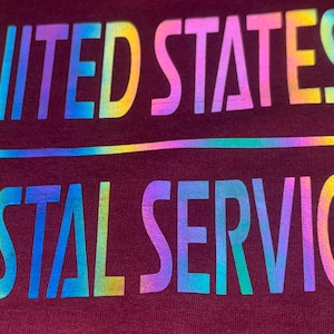 May include: A close-up of a maroon surface with the words "UNITED STATES POSTAL SERVICE" in a rainbow gradient font. A rainbow line separates the two lines of text.