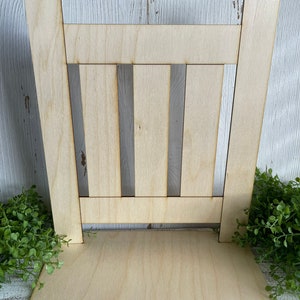 May include: A wooden cutout of a picket fence with a base. The fence is made of light brown wood and has a rustic look.
