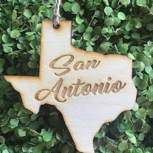 May include: A wooden ornament shaped like the state of Texas with the words "San Antonio" engraved on it.
