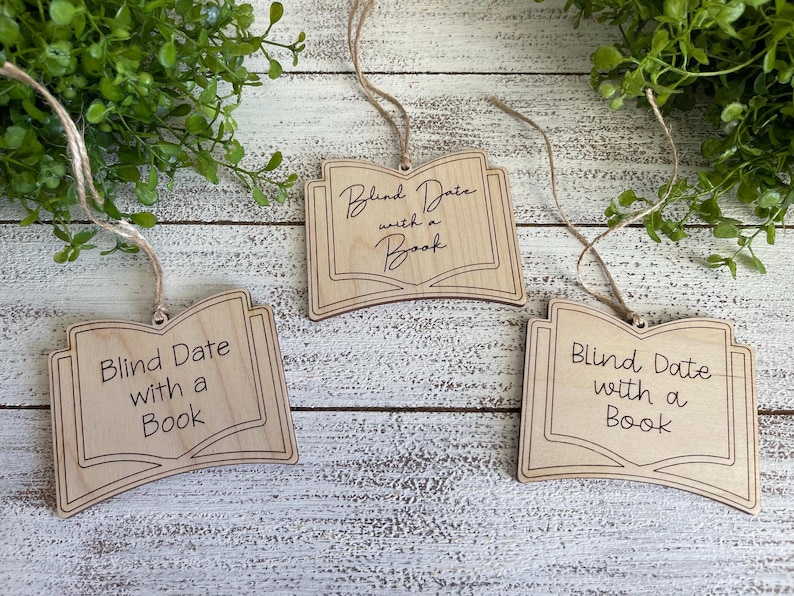 May include: Three wooden book-shaped ornaments with the text "Blind Date with a Book" on each. The ornaments are hanging from twine.