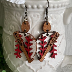 May include: A pair of wooden baseball earrings with red and white accents. The earrings feature a baseball bat and a baseball with the word "Baseball" written on them.