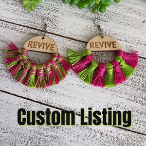 May include: A pair of handmade earrings with green and pink tassels and a wooden circle with the word "REVIVE" engraved on it.