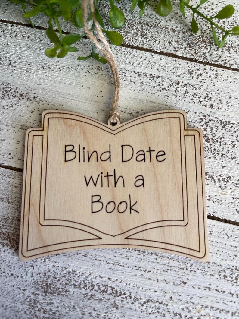 May include: Wooden ornament shaped like an open book with the text "Blind Date with a Book" engraved on it.