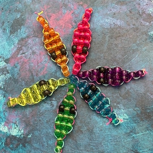 May include: A collection of six beaded insect-like ornaments in a starburst pattern. Each ornament is a different color, including orange, pink, purple, blue, green, and yellow. The beads are strung on a light-colored wire, and each has black beads for eyes.