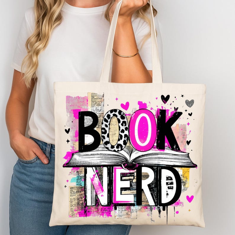 May include: Cream-colored tote bag with the words "BOOK NERD" in a colorful design. The word "BOOK" has a leopard print "O", and the word "NERD" is in white. The design includes an open book and pink accents.