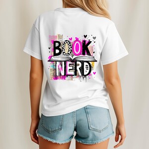 May include: White t-shirt with a colorful graphic that reads "BOOK NERD." The design features an open book with the words above and below it. The letters have a mix of patterns and colors, including leopard print and pink.
