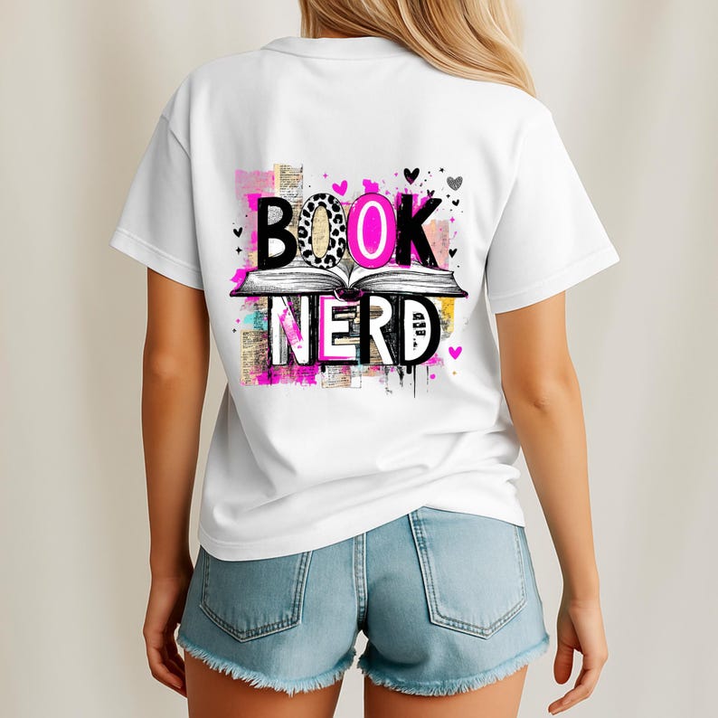 May include: White t-shirt with a colorful graphic that reads "BOOK NERD." The design features an open book with the words above and below it. The letters have a mix of patterns and colors, including leopard print and pink.
