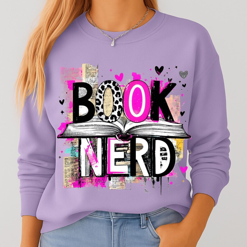 May include: A lilac-colored sweatshirt with the words "BOOK NERD" in a graphic design. The word "BOOK" is above an open book, with the letter "O" in pink and leopard print. Small hearts and abstract shapes are scattered around the design.