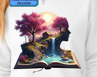 May include: White sweatshirt featuring a vibrant illustration of a landscape scene emerging from an open book. The design includes a waterfall, pink trees, a small cabin, and a silhouette of a face. Text on the top left says "FREE 6 DESIGNS INCLUDES".