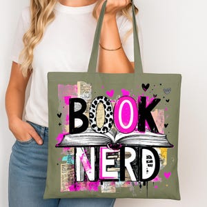 May include: An olive green tote bag with the words "BOOK NERD" in a bold, colorful design. The word "BOOK" features a leopard print "O", and the word "NERD" is in white. The design includes an open book and pink accents.