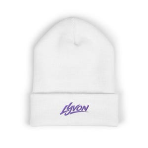 Peut inclure: Un bonnet blanc avec un bord replié. Le mot "LYVON" est brodé en violet sur le devant. Le bonnet est fait d'une matière tricotée douce.