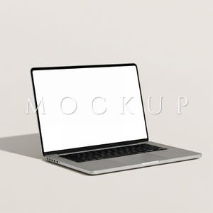 May include: A silver laptop with a black keyboard and a blank white screen. The word "MOCKUP" is displayed on the screen. The laptop is angled slightly to the right, casting a shadow on the white surface.