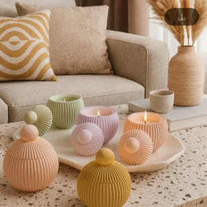 May include: A collection of colorful, decorative candles in various pastel shades, including pink, green, and yellow. The candles are in round, ribbed containers with matching lids. Some candles are lit, and the scene is set on a coffee table.