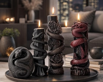 May include: A collection of decorative candles with snake and rose designs. The candles are black and burgundy, with lit flames. One candle features a coiled snake, while others have snakes entwined with roses. The candles sit on a dark tray.