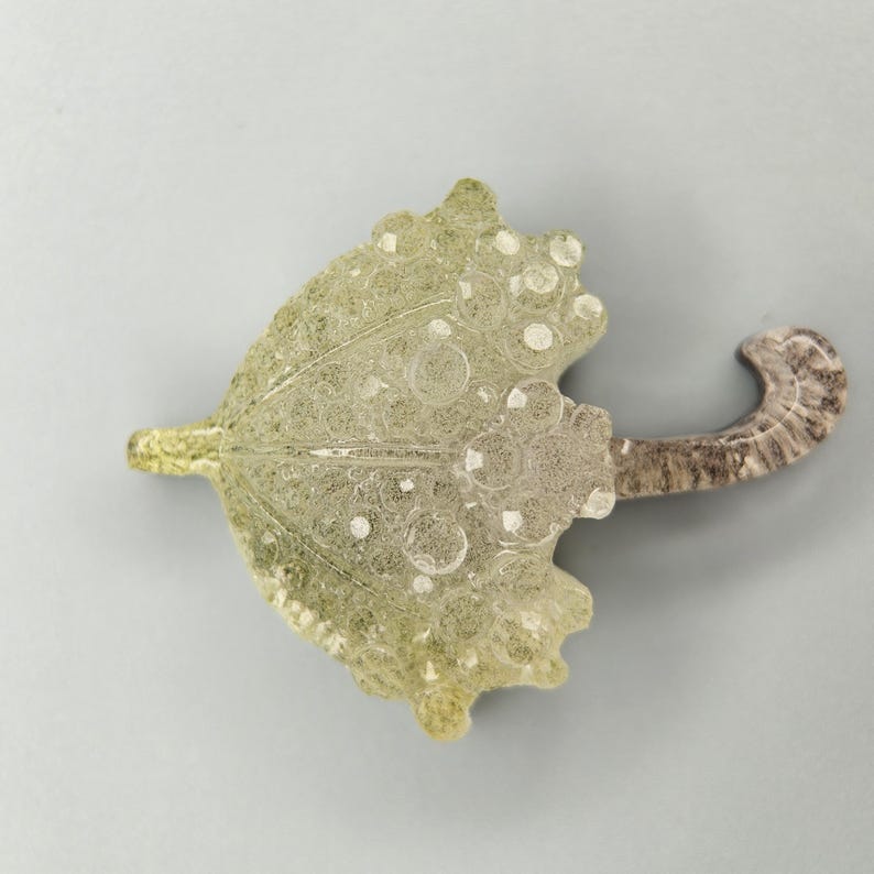 Op de afbeelding: Een decoratief parapluvormig object met een lichtgroen en transparant ontwerp. De paraplu heeft een gebogen handvat met een gemarmerd uiterlijk. De bovenkant van de paraplu heeft een textuurpatroon met cirkelvormige details.