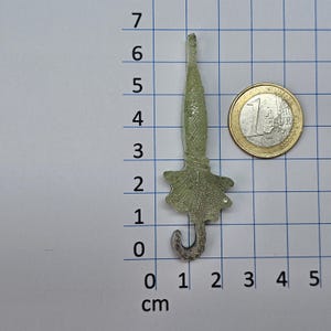 Puede incluir: Un dije de paraguas de vidrio verde claro con un asa curvada. Una moneda de un euro est&aacute; al lado del dije para comparar el tama&ntilde;o. El paraguas mide aproximadamente 2,5 cm de largo.