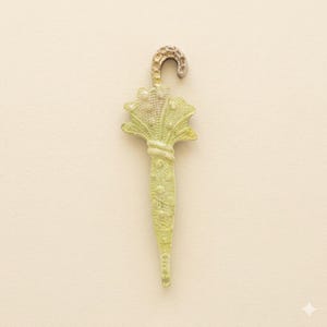 Puede incluir: Un peque&ntilde;o dije decorativo de paraguas en un tono verde p&aacute;lido con un asa plateada. El dise&ntilde;o del paraguas presenta detalles intrincados, incluyendo un asa texturizada y un dosel detallado. El dije es probablemente de metal y es adecuado para joyer&iacute;a o proyectos de manualidades.