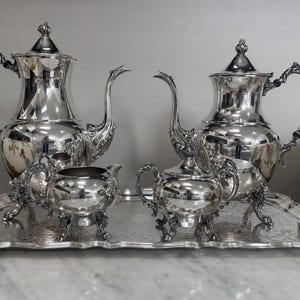 May include: A polished silver tea set comprising two teapots, a creamer, and a sugar bowl, presented on a decorative tray. The reflective surfaces of the tea set create a bright and elegant display, ideal for serving tea.